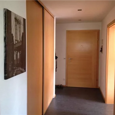 Ein Flur mit Holzberichten und einer grauen Wand. An der Wand hängt ein Bild einer Brücke.