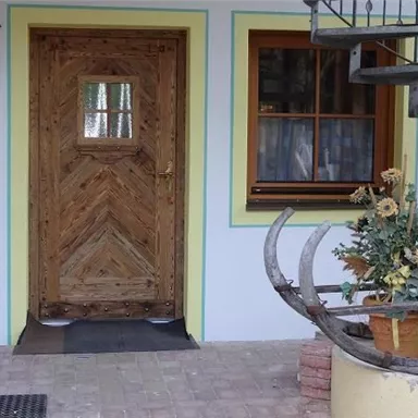 A rustic wooden door with a beautiful pattern and a window beside it. In front of the door stands a flower pot with colorful flowers.