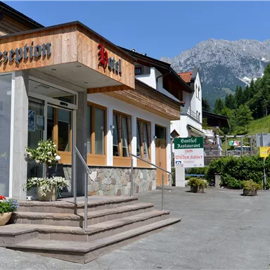 Ein einladendes Hotel mit Holzverkleidung und einer schönen Eingangstreppe. Im Hintergrund sind grüne Berge und eine klare blaue Himmel sichtbar.