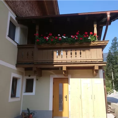 A beautiful house with a balcony decorated with red flowers. The sky is clear and blue, creating a sunny atmosphere.