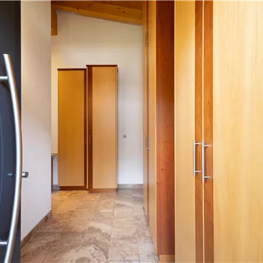A modern designed hallway with large wooden cabinets visible from the entrance door. The floor is made of light tiles and the walls are in neutral tones.
