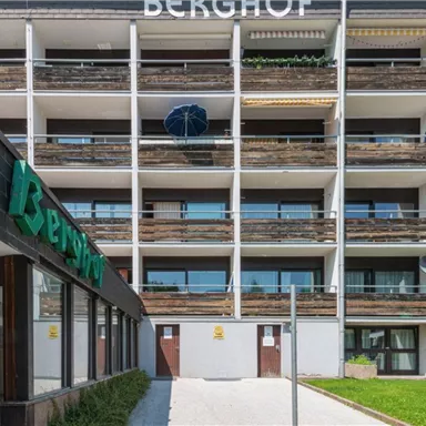 Ein modernes Gebäude mit dem Namen "Berghof". Die Fassade hat mehrere Balkone und ist von Grünflächen umgeben.
