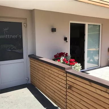 A modern entrance to a building with the inscription "wittner's".
Flowers in colorful boxes adorn the area in front of the door.