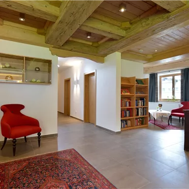 An inviting entrance area with modern furniture and wooden ceilings. Red accent chairs and bookshelves create a cozy atmosphere.