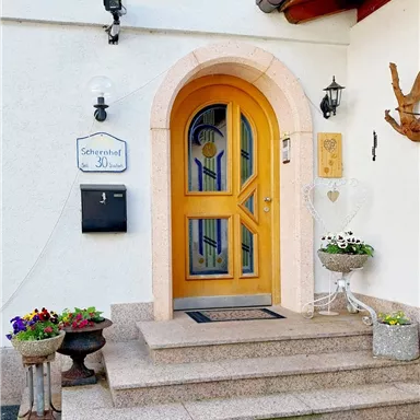 Eine einladende Haustür mit einem bogenförmigen Rahmen in warmem Holzton. Dazu gehören Blumenbehälter und eine entspannte Atmosphäre.