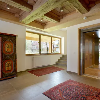 An inviting entrance area with large windows and wooden beams on the ceiling. A decorative cabinet and rugs give the room character.
