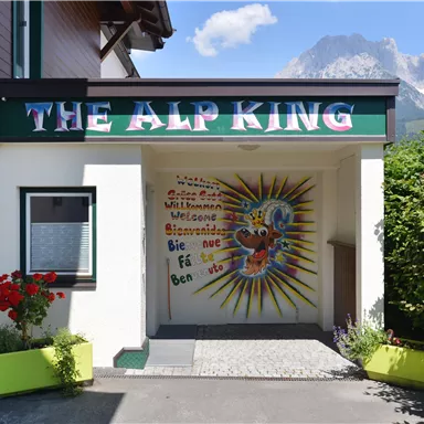 An entrance to a building with the inscription "The Alp King". The wall is colorfully designed and features a friendly greeting.