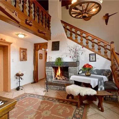 Ein gemütlicher Wohnraum mit einer Treppe aus Holz und einem Kamin. Die Einrichtung ist rustikal, mit einer schönen Pflanze und dekorativen Elementen.