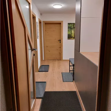 Ein einladender Flur mit Holztüren und einem hellen Boden. Auf der linken Seite sind Matten und ein Haken für Mäntel.