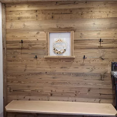A bright wooden wall with a central wall decoration and several hooks. Below is a simple wooden bench.  
Cordless vacuum cleaner available.