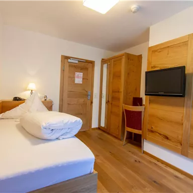 A simple room with a single bed and wooden details. There is a television and a small table with a chair.