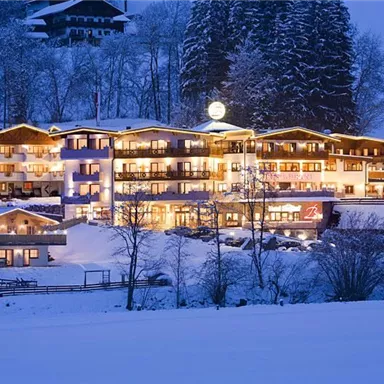 A picturesque hotel amidst a winter landscape. It is illuminated and surrounded by snow and trees.