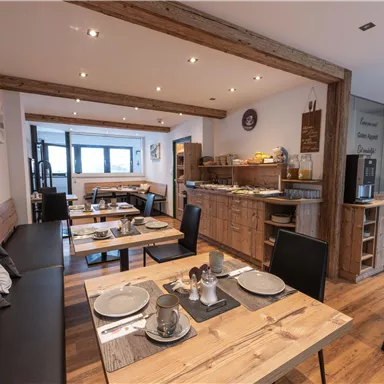 An inviting restaurant with wooden interior and cozy tables. The space is bright and has a breakfast buffet area.