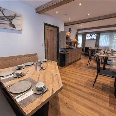 A cozy restaurant with wooden tables and chairs. The walls are painted light and decorated with photos.