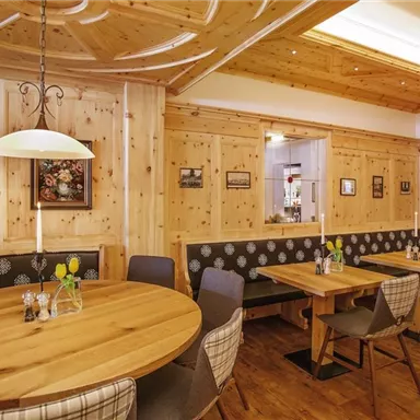 A cozy restaurant with warm wood design and round tables. The walls are decorated with artworks and pictures.