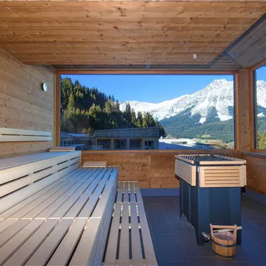A beautiful sauna area with wooden benches and a window that overlooks snow-covered mountains. The atmosphere exudes calm and relaxation.