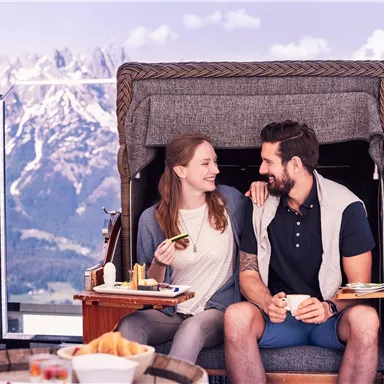 A couple is sitting in a cozy beach chair with a view of the mountains. They are smiling at each other and enjoying their time together.