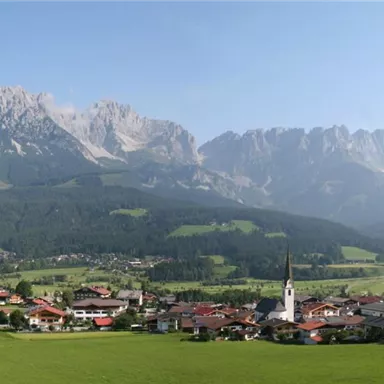A picturesque mountain landscape with impressive peaks in the background. In the foreground lies a small village in a green valley.