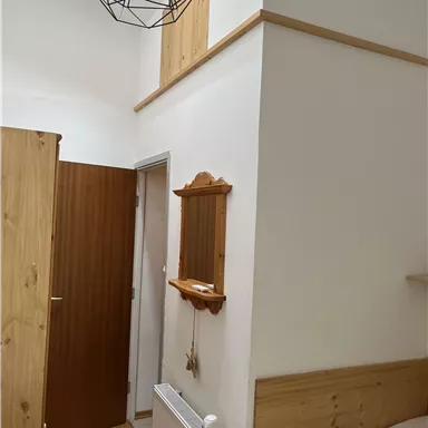 Ein moderner Raum mit Holzdetails und einer klaren Gestaltung. Die Decke ist mit einer geometrischen Lampe dekoriert und es gibt mehrere Türen.