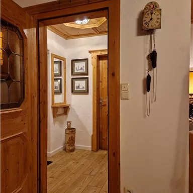An inviting entrance area with wooden doors and a rustic design. Pictures and a classic clock hang on the wall.