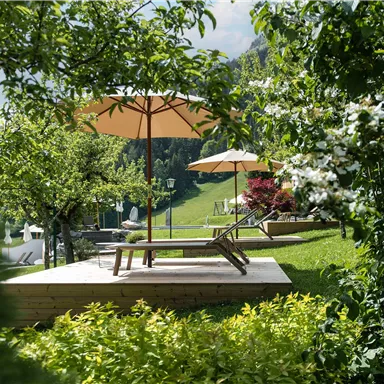 Ein schöner Garten mit Liegen und Sonnenschirmen, umgeben von grünen Pflanzen. Der Blick reicht über eine sanfte Hügelkette.