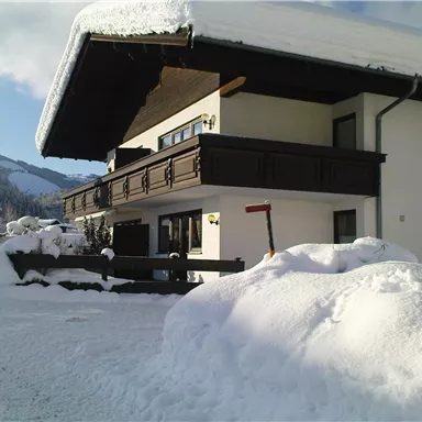 A charming house in the snow with a overhanging roof. The surroundings are wintry and picturesque with snow-covered trees.