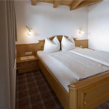 Ein gemütliches Schlafzimmer mit einem Doppelbett und zwei großen Kissen. Die Holzdecke und die sanfte Beleuchtung schaffen eine einladende Atmosphäre.