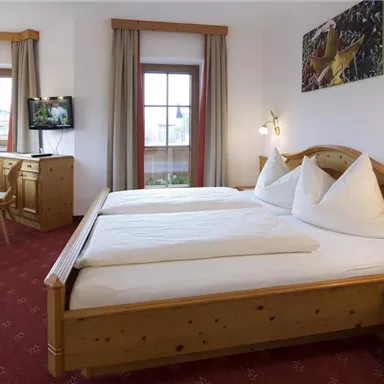 Ein gemütliches Zimmer mit einem Doppelbett und Holzdetails. Große Fenster sorgen für viel Licht und eine angenehme Atmosphäre.