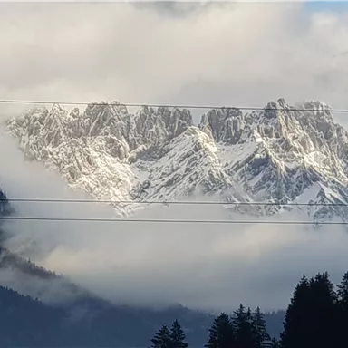 Schneebedeckte Berge ragen aus dichtem Nebel. Die Landschaft zeigt eine dramatische Aussicht mit Wolken und Schatten.