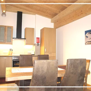 A modern kitchen with wooden shelves and a dining table. The decor is cozy and inviting.