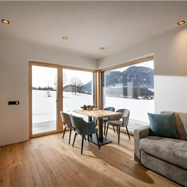 A cozy living area with a table and chairs, large window overlooking the snowy landscape. The interior is bright and modernly designed.