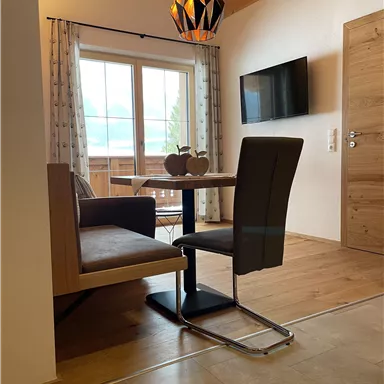 A cozy dining area with a table, a chair, and a bench. Large windows let in plenty of daylight and provide a lovely view outside.