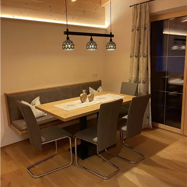 A cozy dining area with a wooden dining table and modern chairs. The lighting creates a warm atmosphere.