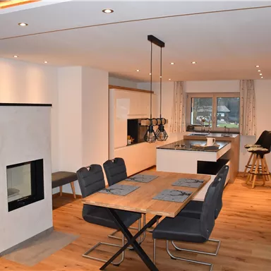 A modern kitchen with a dining area and a fireplace. The room is bright and inviting, with wooden flooring and elegant furniture.