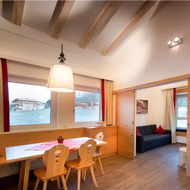 Eine gemütliche Wohnküche mit einem Tisch und Stühlen. Der Raum hat große Fenster mit Blick auf die Umgebung und ist hell und freundlich gestaltet.