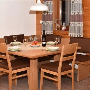 Ein gemütlicher Essbereich mit einem Holztisch und Stühlen. Der Tisch ist schön gedeckt und es gibt eine Flasche Wein sowie Obst in der Mitte.