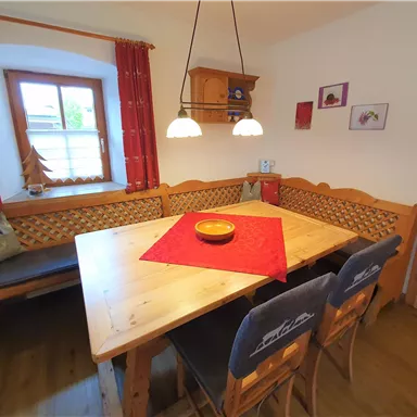 A cozy dining area with a large wooden tray and a red tablecloth. The walls are cheerfully decorated with windows and decorative elements.
