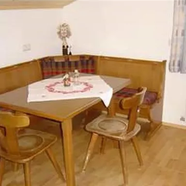 Ein gemütlicher Essbereich mit einem Holztisch und Stühlen. Die Wände sind schlicht und die Fenster lassen viel Licht herein.