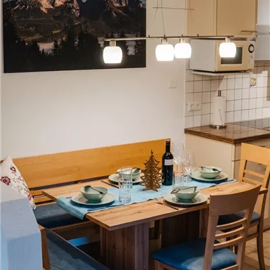 A cozy dining area with a wooden table and chairs. A picture of mountains hangs on the wall, and the table is nicely set.