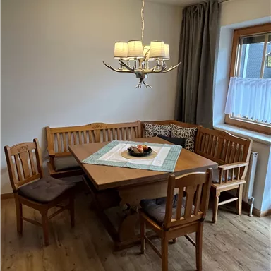 A cozy dining area with a wooden table and benches. A modern lamp hangs from the ceiling, and a window provides plenty of light.