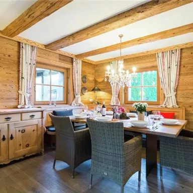 Ein gemütlicher Essbereich mit Holzwänden und einem großen Tisch. Dazu dekorierte Stühle und eine stilvolle Deckenleuchte.