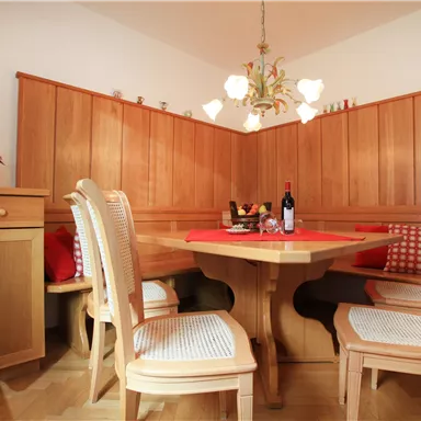 A cozy dining area with wooden paneling and a rustic table. On the table are wine and fruit, complemented by comfortable chairs.