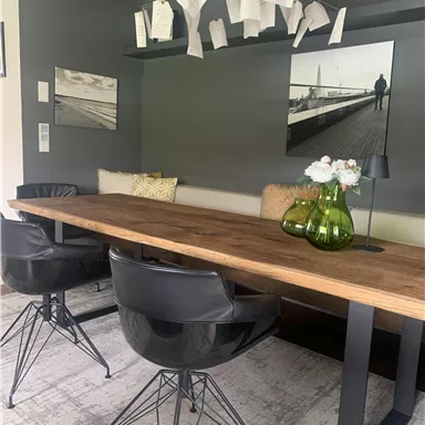 Ein moderner Essbereich mit einem großen Holztisch und schwarzen Stühlen. An der Decke hängen Zettel, und auf dem Tisch stehen dekorative Vasen mit Blumen.