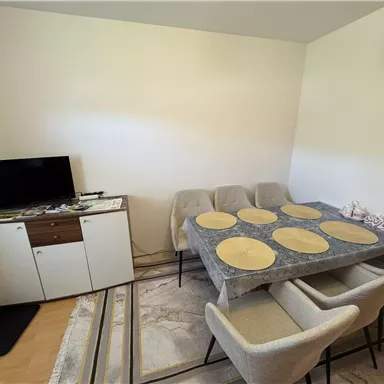 A modern dining area with an elegant table and chairs. In the background, there is a television and a sideboard.