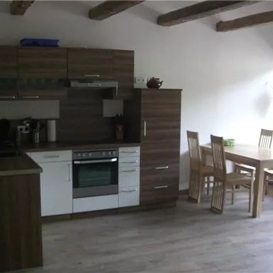 A modern kitchen with wooden shelves and a dining table group. The space is bright and inviting, with a clear and functional design.