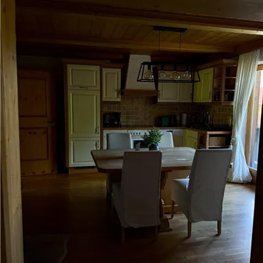 A cozy kitchen with a wooden table and modern chairs. The decor is bright and inviting, with large windows that let in daylight.