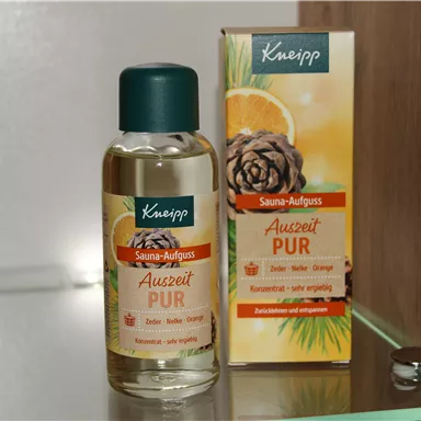 A small bottle of sauna extract from Kneipp is next to a packaging. The product is labeled "Auszeit PUR" and contains essential oils.