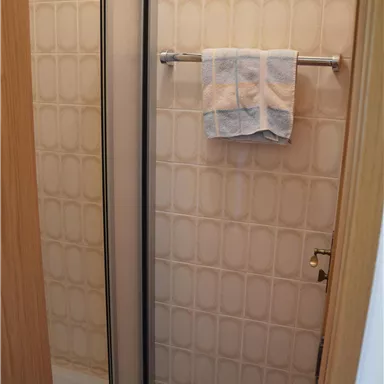 A small bathroom with a shower and a towel. The walls are designed in a light, patterned style.