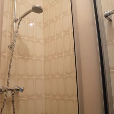 A shower with a clear shower wall. The walls are decorated with light tiles.