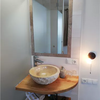Ein modernes Badezimmer mit einem stilvollen Waschbecken aus Stein. Der Holzregal bietet Platz für Handtücher und Pflegeprodukte.